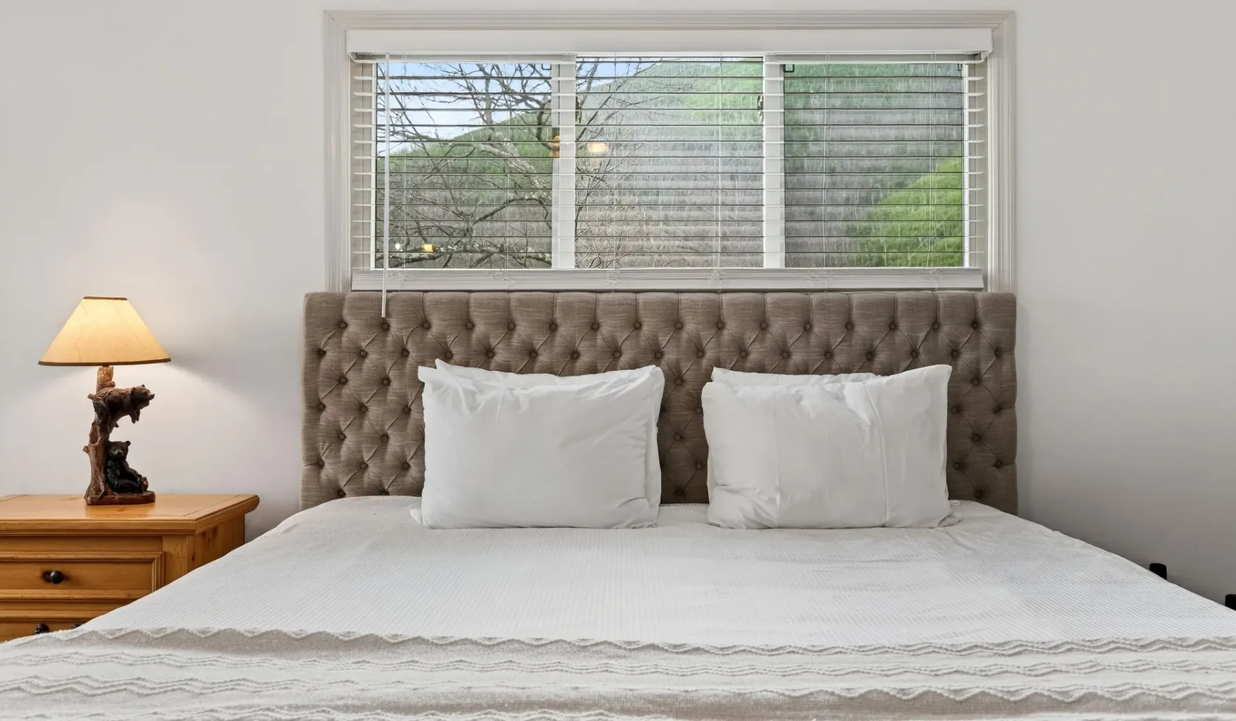 Un dormitorio con una cama bien arreglada y una ventana sobre el cabecero.
