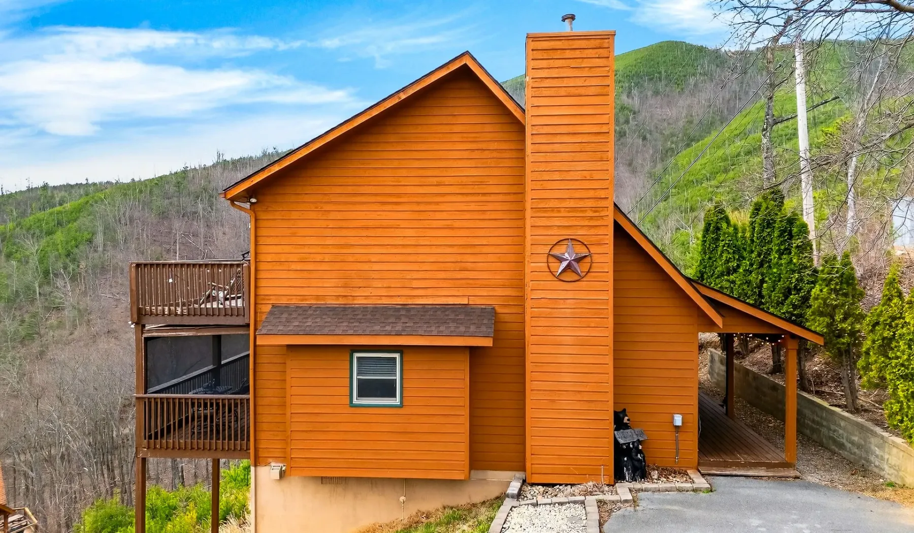Una cabaña de revestimiento naranja se alza en una ladera arbolada junto a una entrada pavimentada.