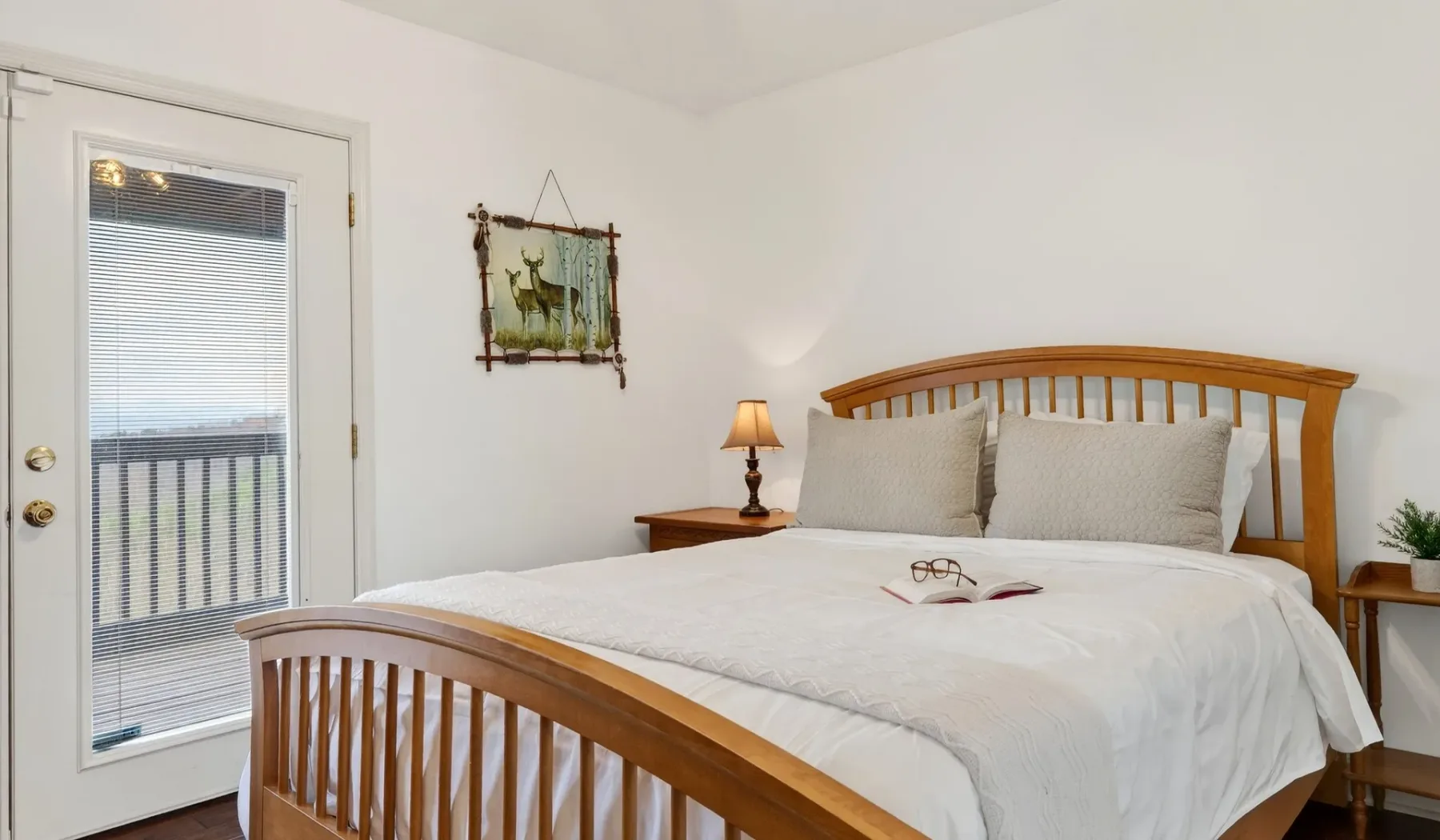 Un dormitorio luminoso con una cama de madera, ropa de cama blanca y una puerta de vidrio.