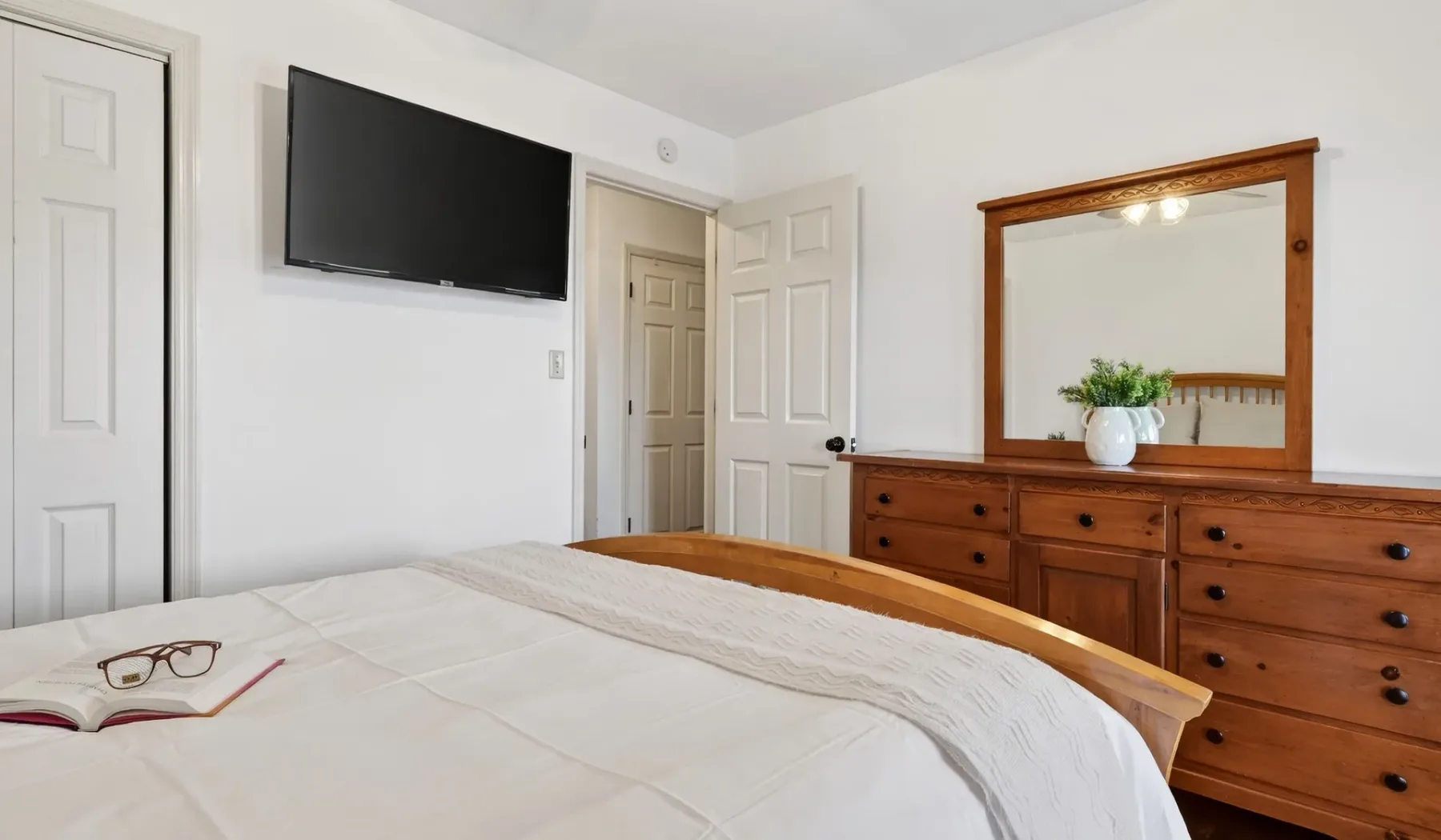 Un dormitorio con una cama bien tendida, un televisor en la pared y una cómoda de madera.