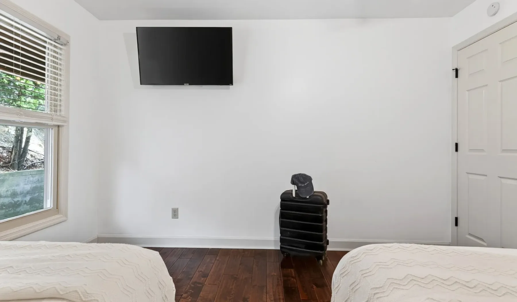 Un dormitorio luminoso con dos camas, un televisor en la pared y una ventana.