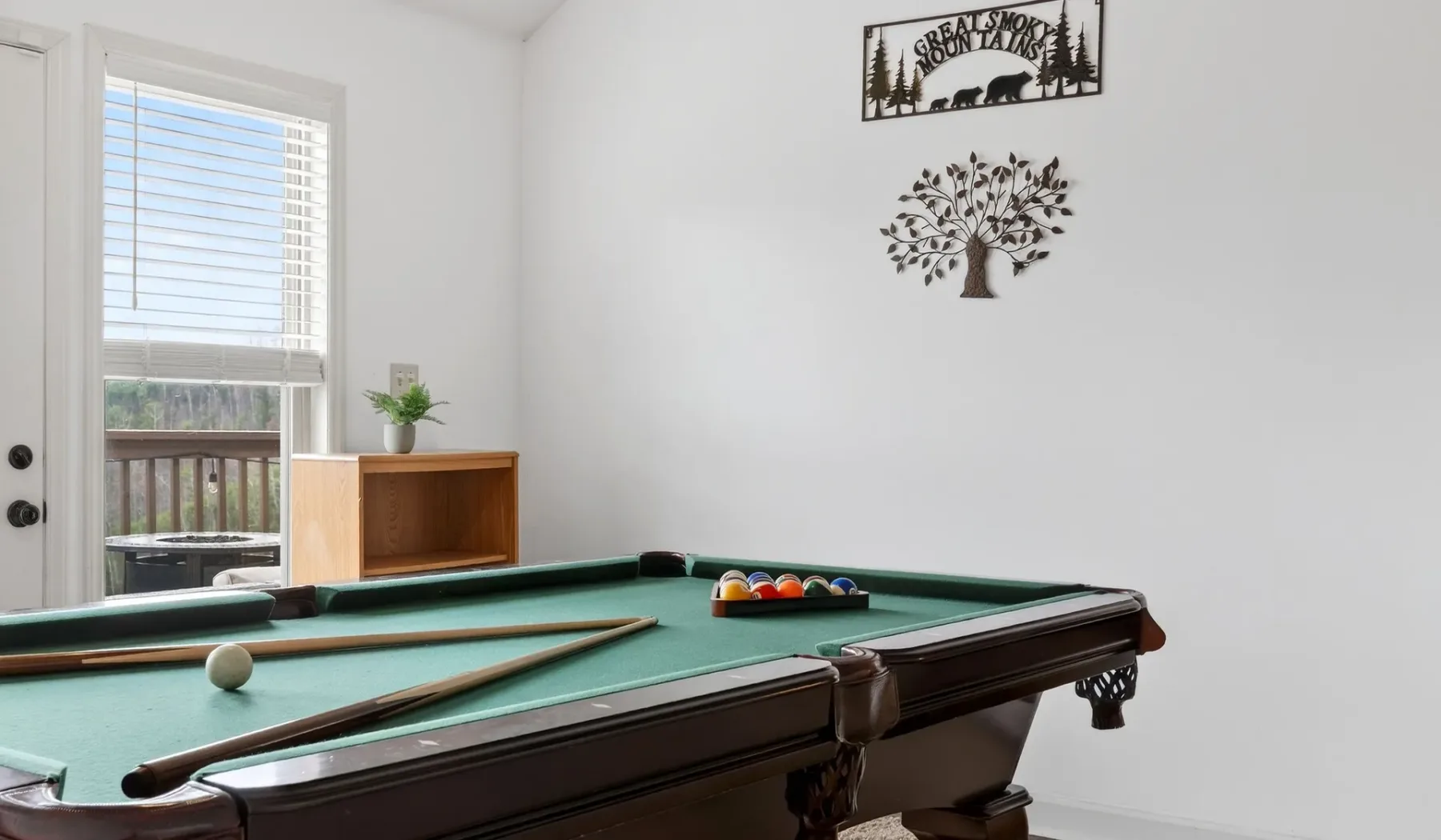Una mesa de billar ocupa una habitación luminosa, con una ventana y adornos en la pared.