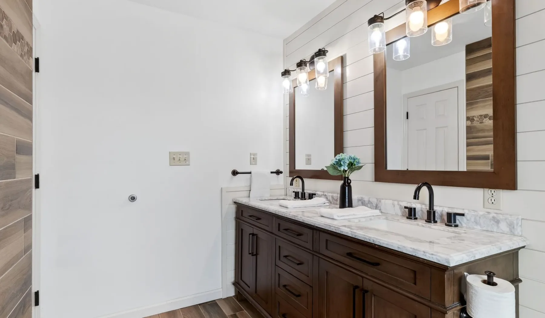 Un tocador de baño con muebles oscuros, encimera de mármol y espejos grandes.