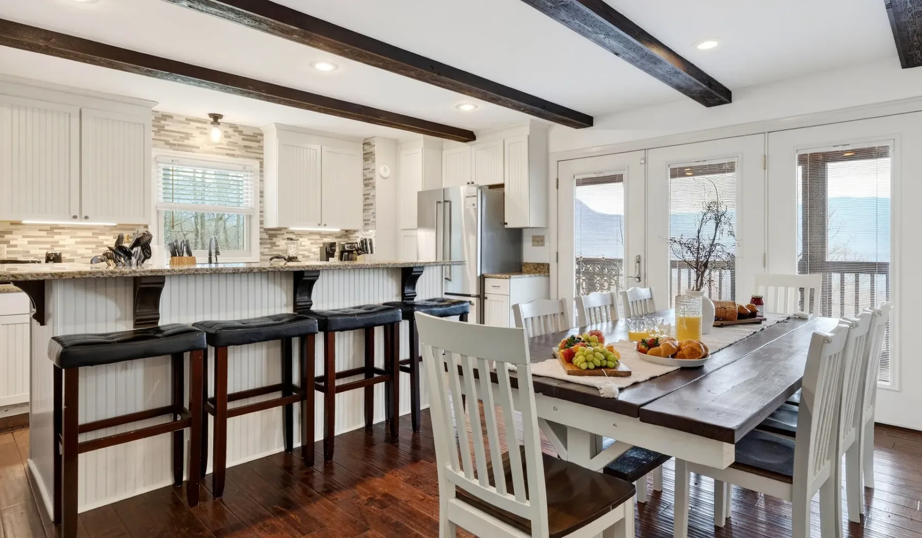 Una luminosa cocina con comedor y una mesa larga junto a grandes ventanas.