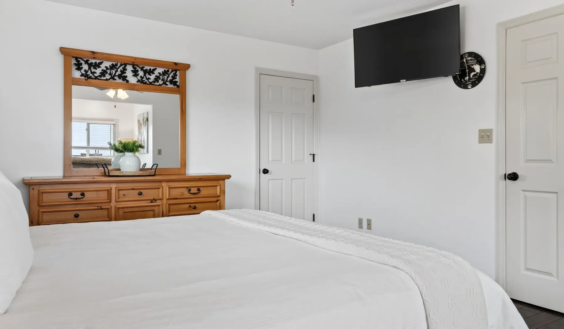 Un dormitorio con una cama bien tendida, una cómoda de madera y un televisor en la pared.