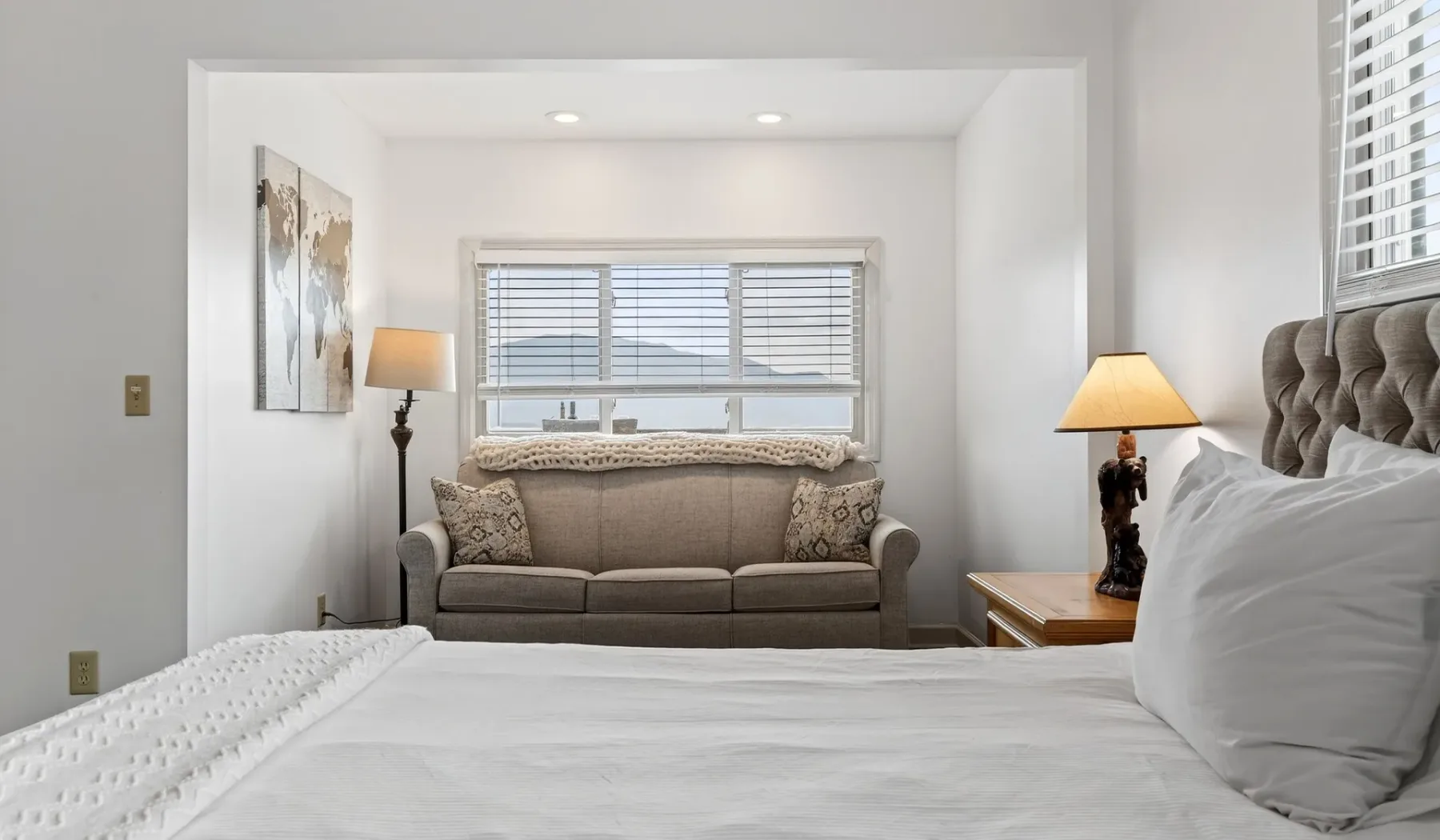 Un dormitorio luminoso con una cama en primer plano y un sofá junto a la ventana.