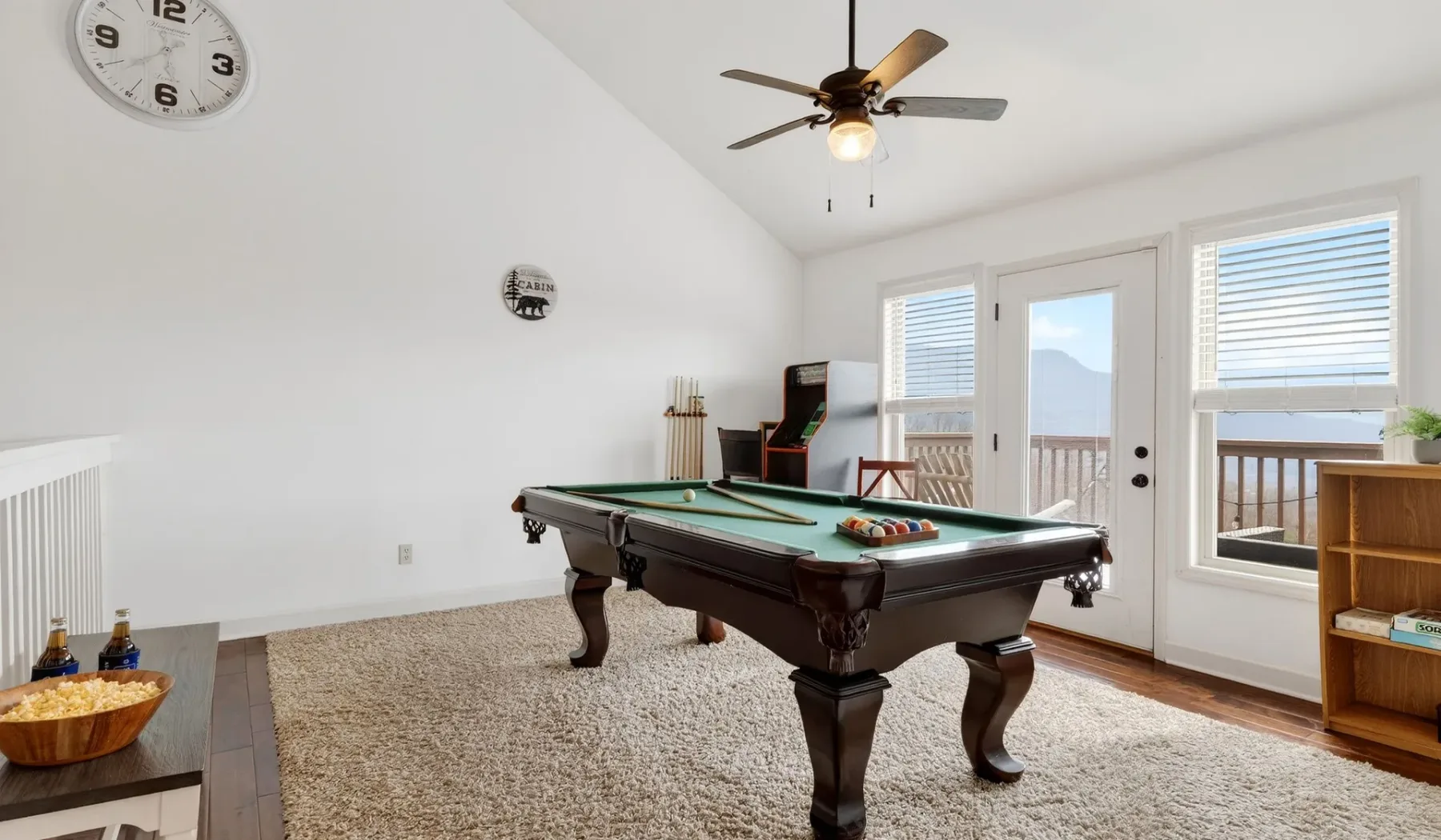 Una sala de juegos con una mesa de billar, un ventilador de techo y ventanas con vista a un balcón.