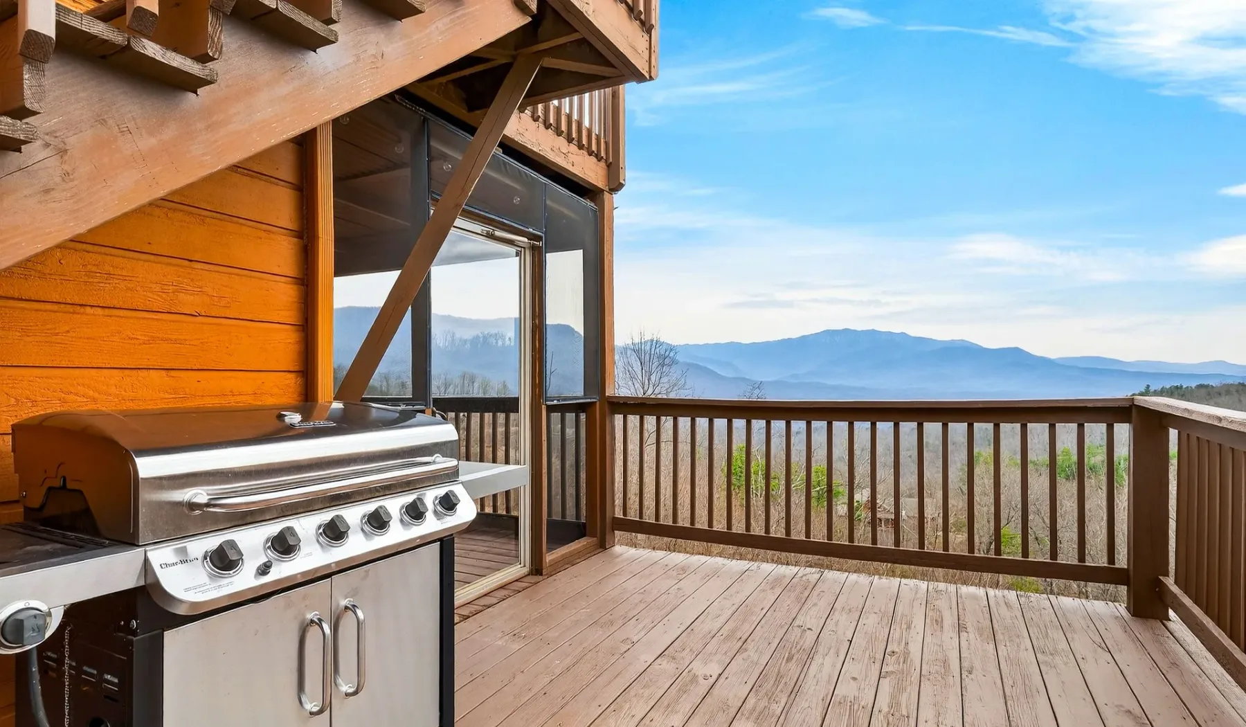 Una terraza de madera con una parrilla ofrece vistas a una cadena montañosa.