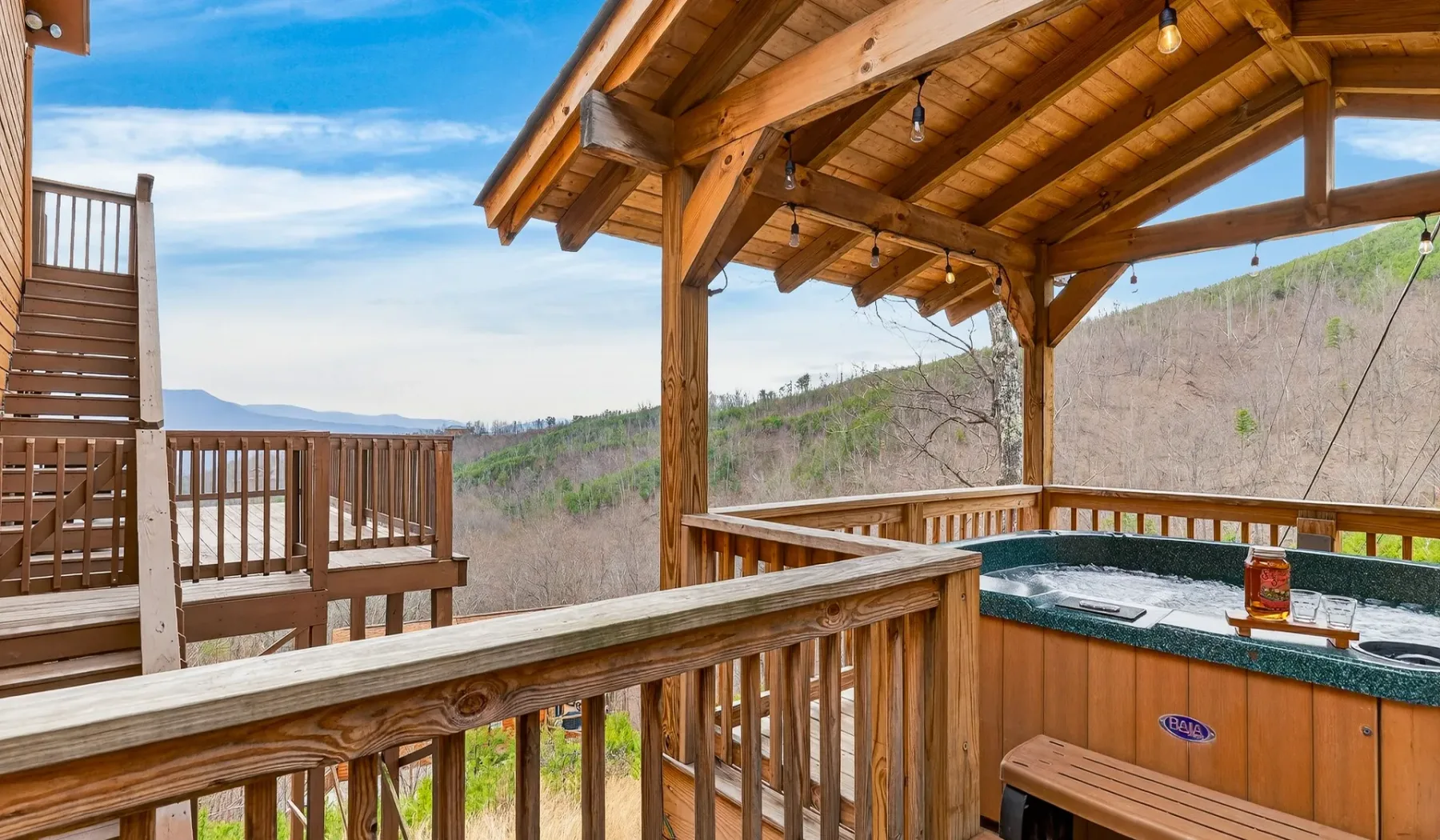 Una terraza de madera cubierta con jacuzzi da a una ladera boscosa.