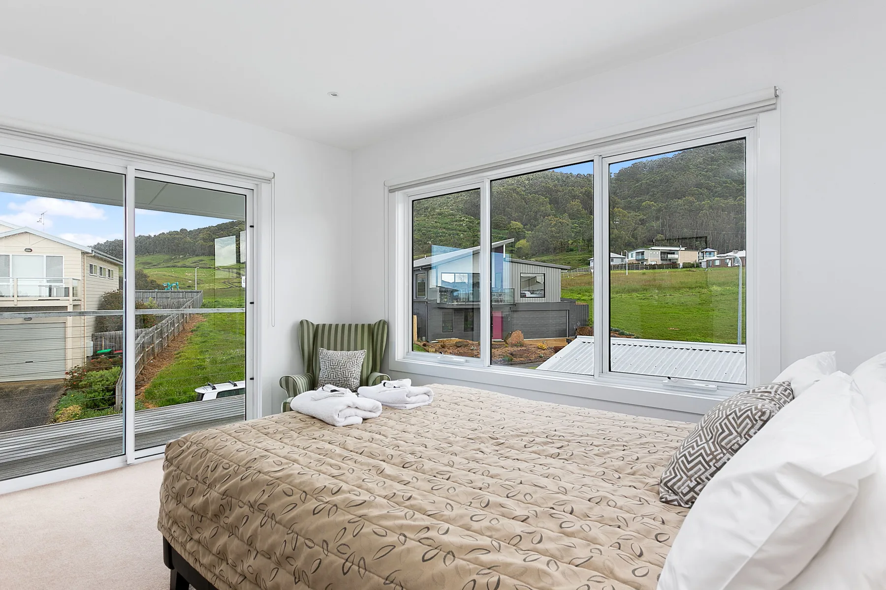 A bright bedroom with a bed and large windows overlooking a green hillside.