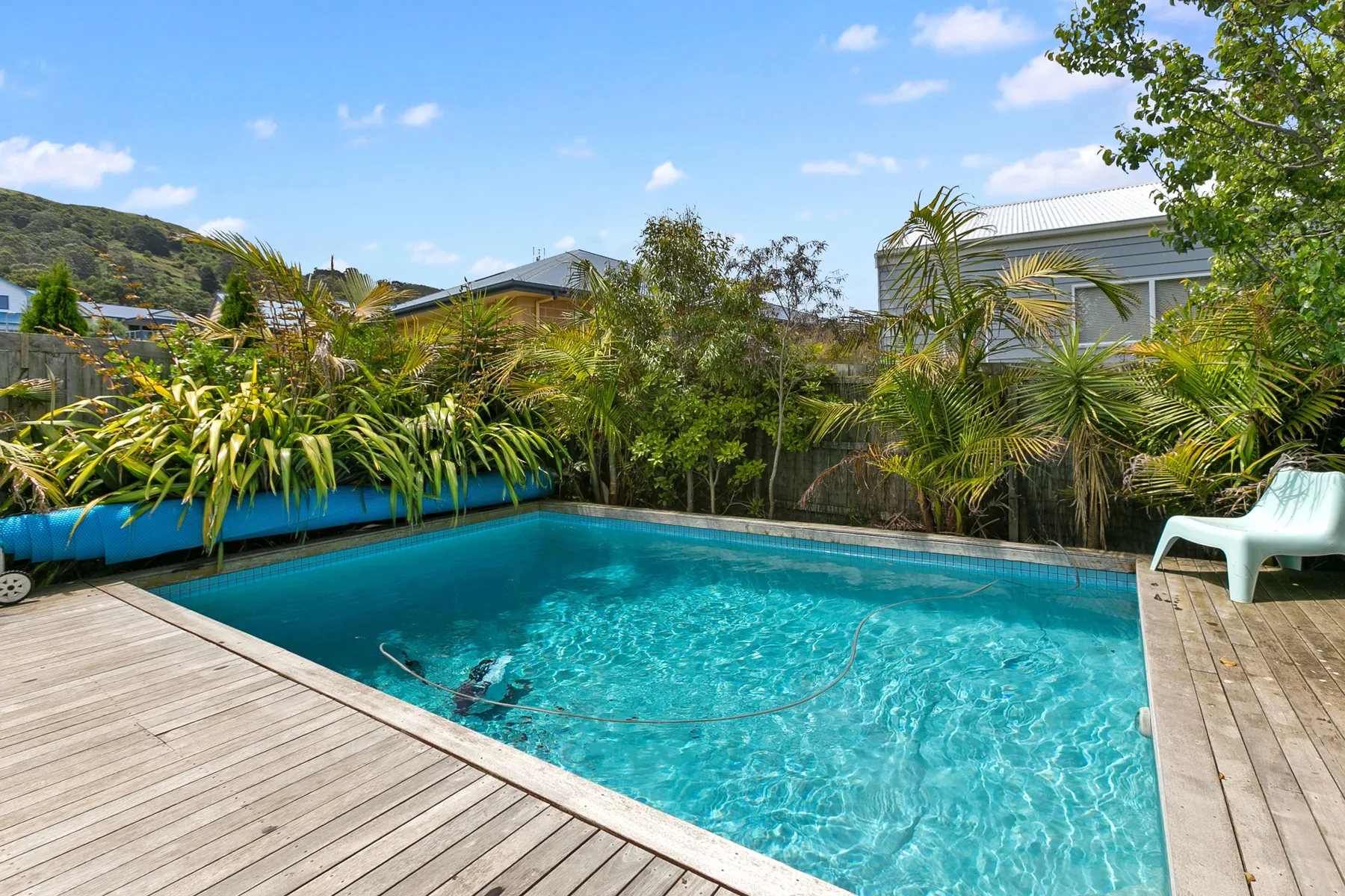 Una piscina al aire libre está rodeada de tarima de madera y plantas tropicales.