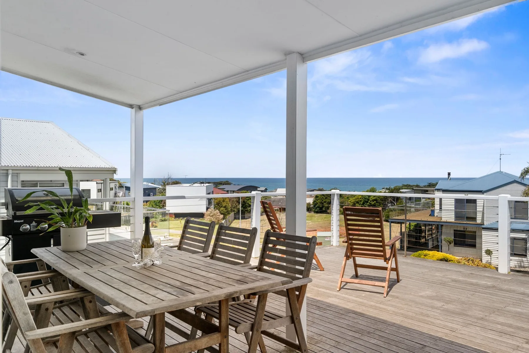 A covered outdoor deck has a dining table, seating, and a view of the ocean.