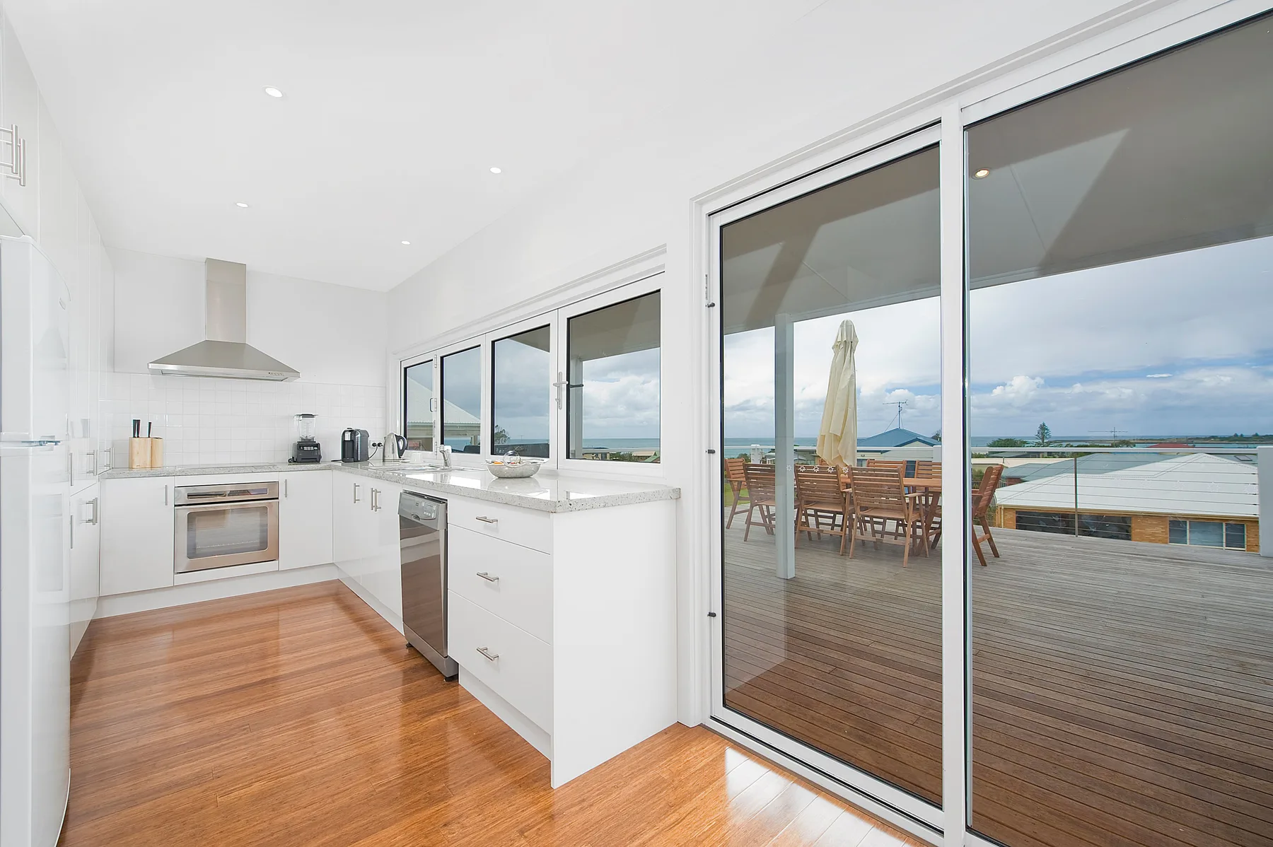 A bright kitchen opens onto a deck with outdoor dining furniture and a water view.