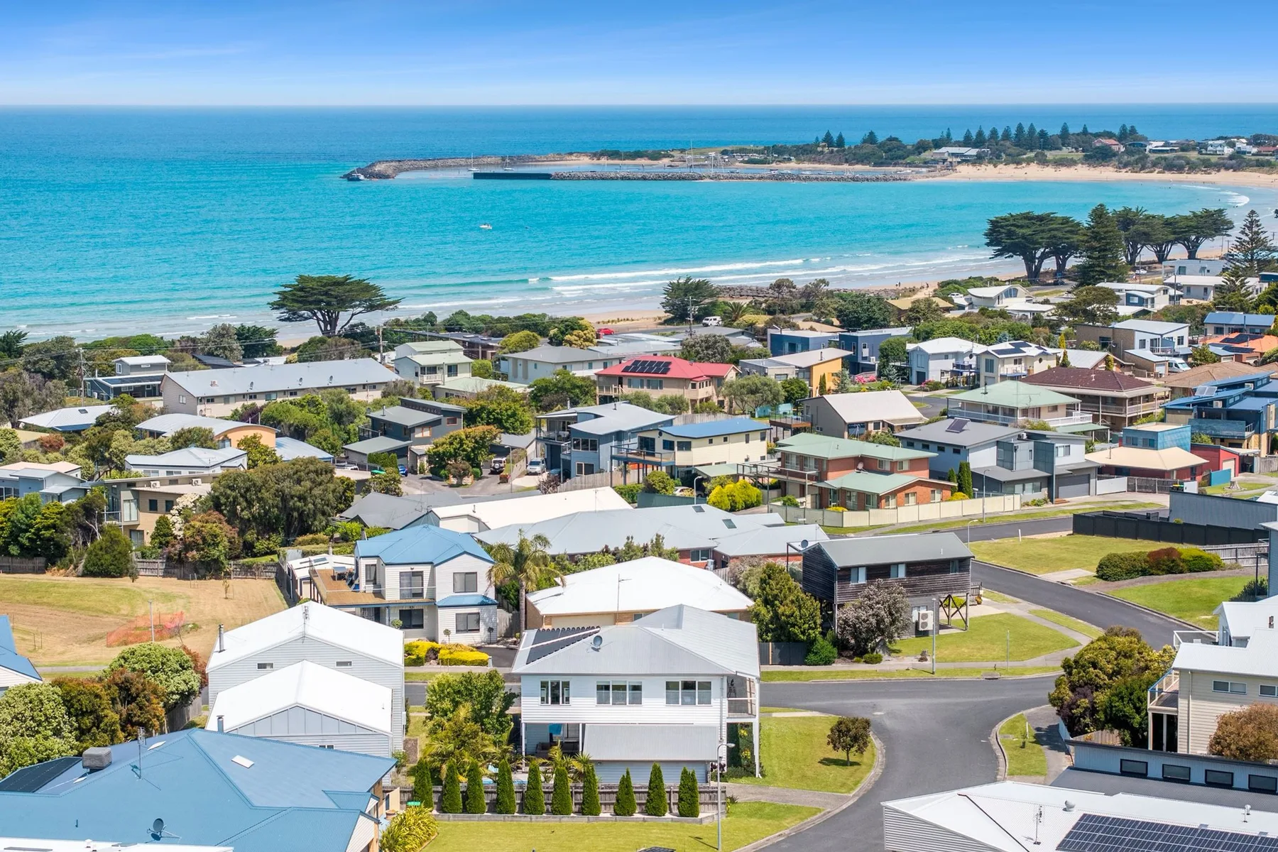 Coastal neighborhood with homes beside a sandy beach and blue ocean.