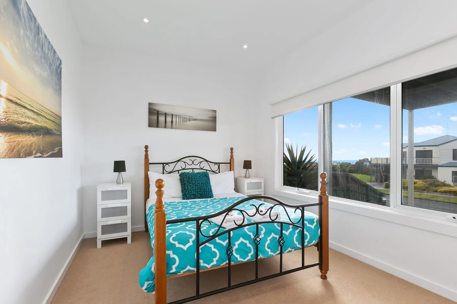Un dormitorio luminoso con una cama estampada junto a grandes ventanas.
