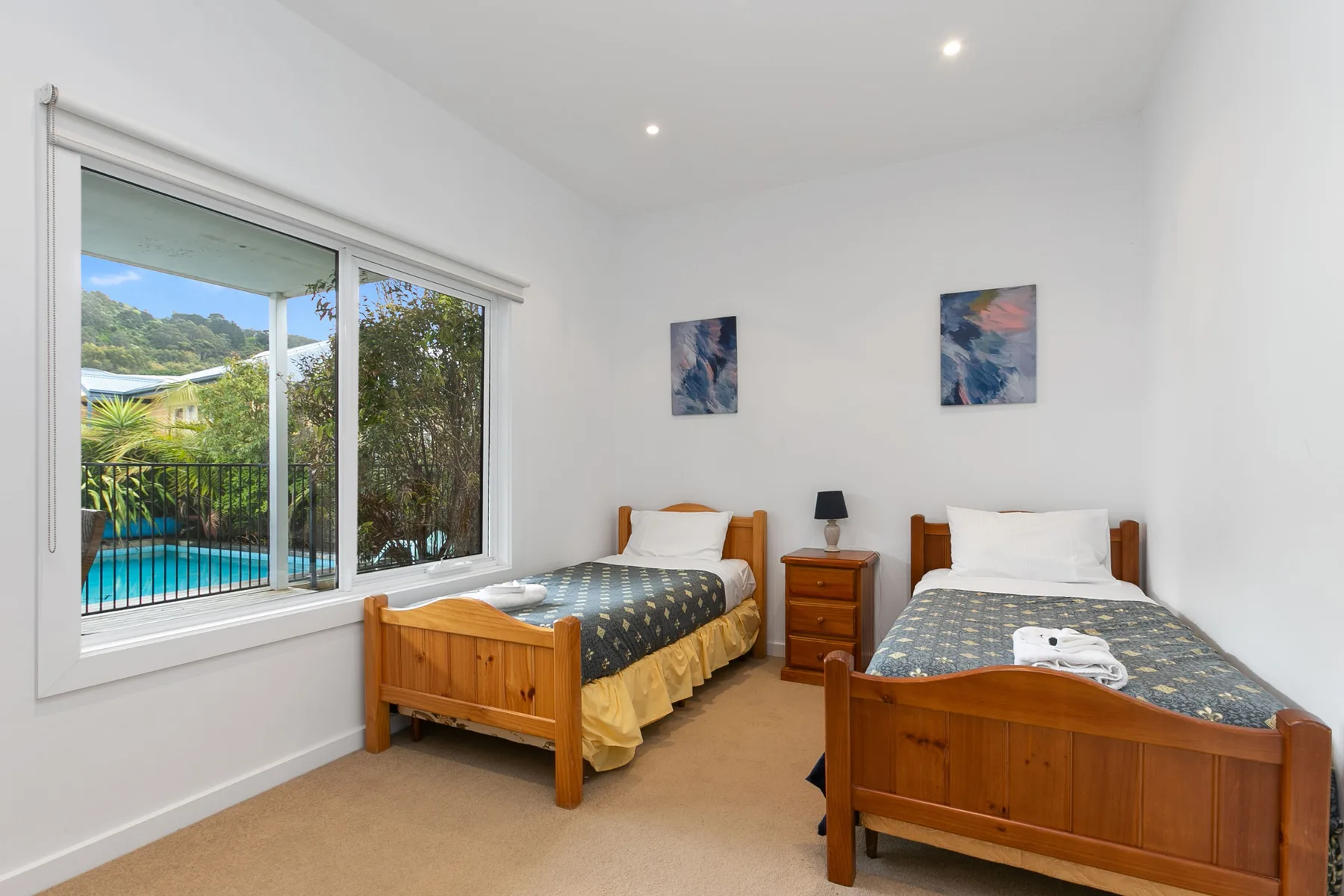 Un dormitorio luminoso con dos camas y una gran ventana con vistas a una piscina.