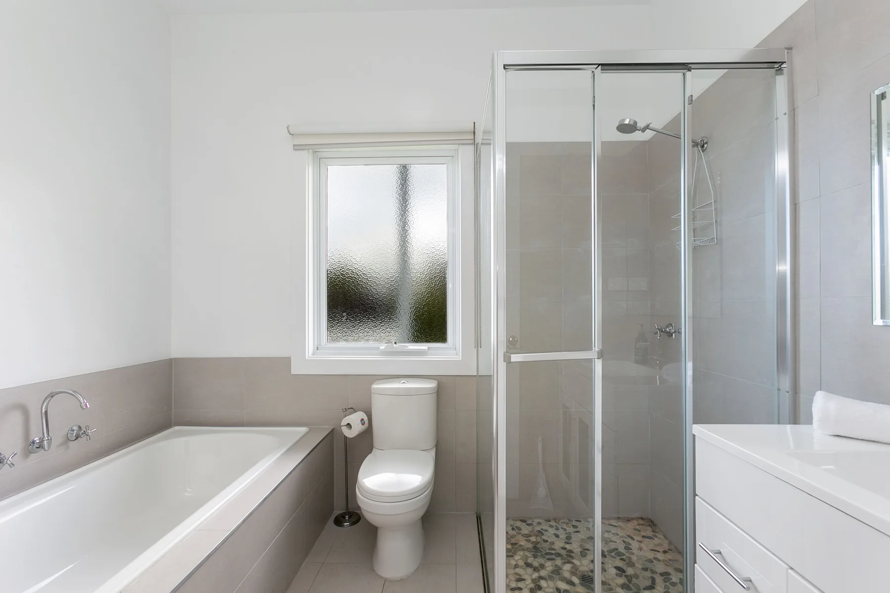 A bright bathroom with a bathtub, toilet, and glass-enclosed shower.