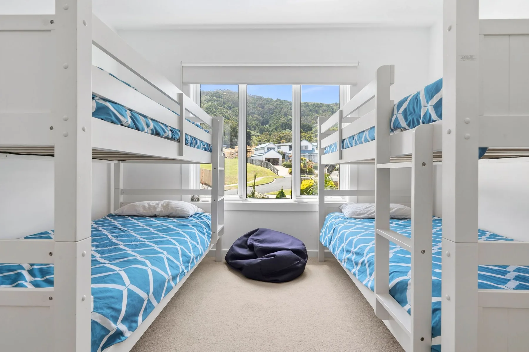 A bright bunk room with blue patterned bedding and a large window.