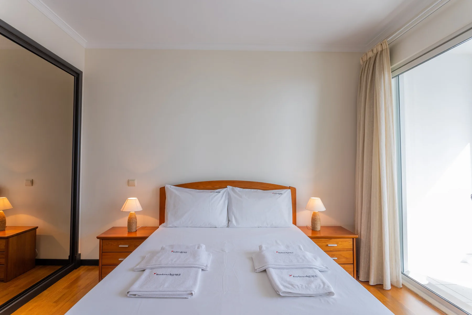 A bedroom with a neatly made bed, bedside tables, and a large window.