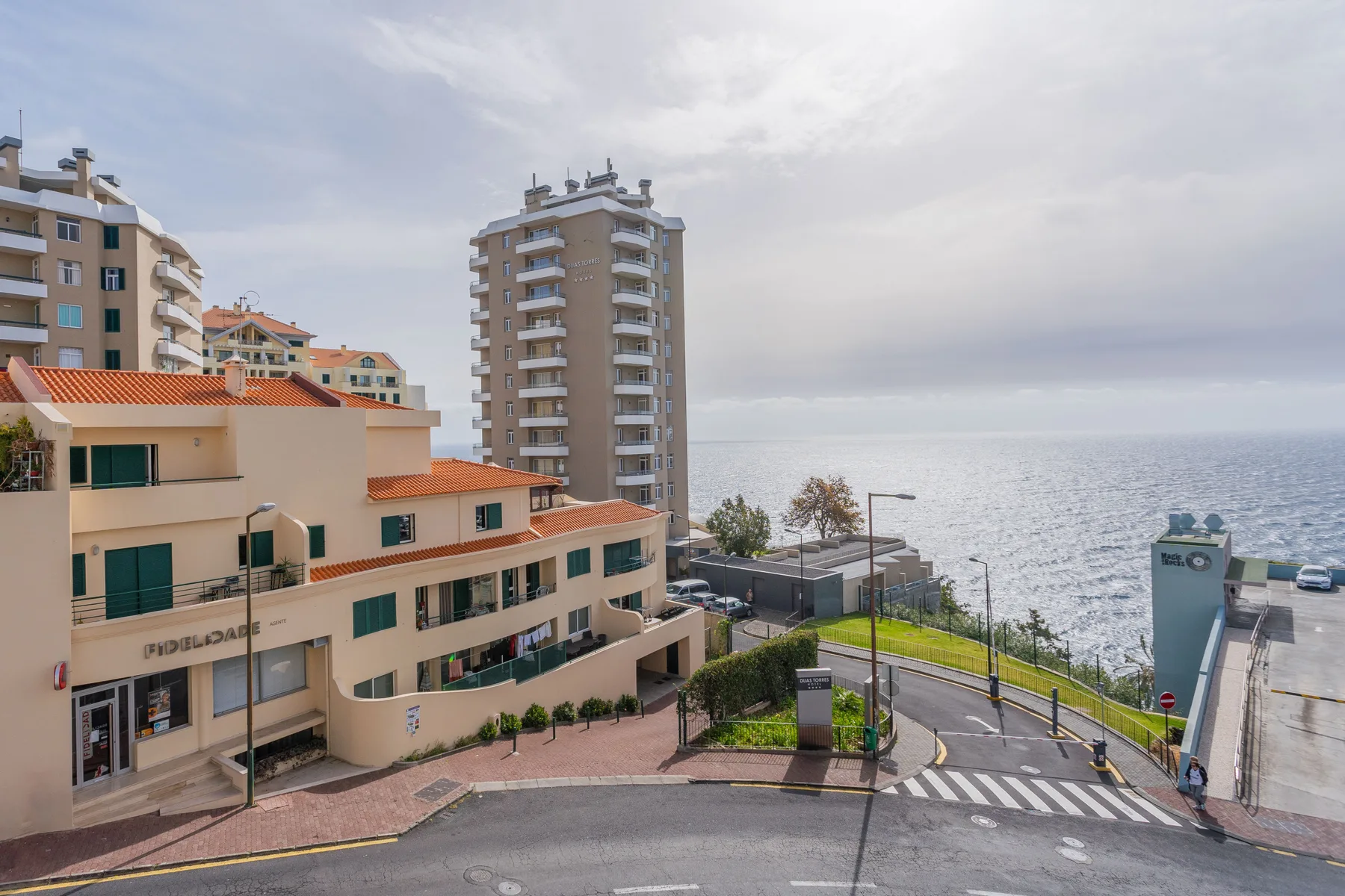 A coastal street curves past apartment buildings beside the sea.