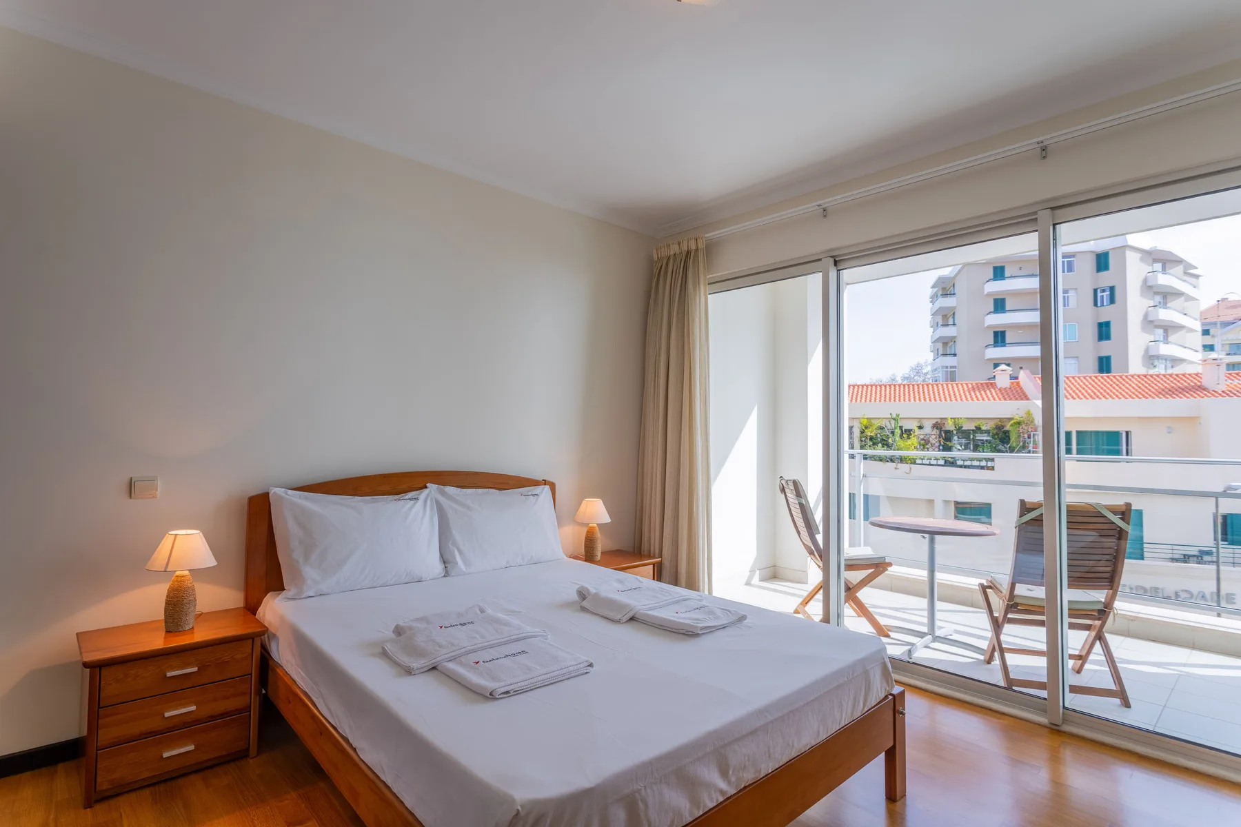 A bedroom with a neatly made bed beside sliding glass doors opening onto a balcony.