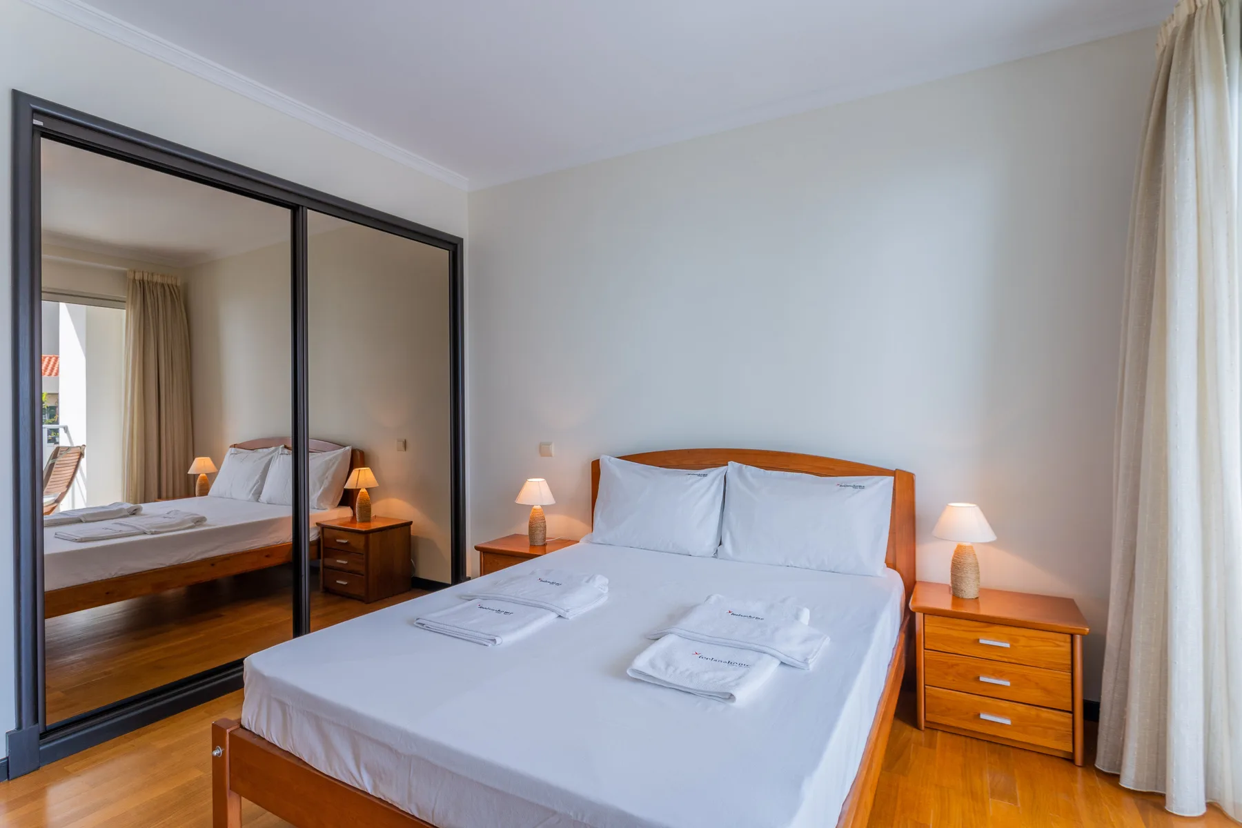 Un dormitorio con una cama, mesitas de noche y puertas de armario con espejo.
