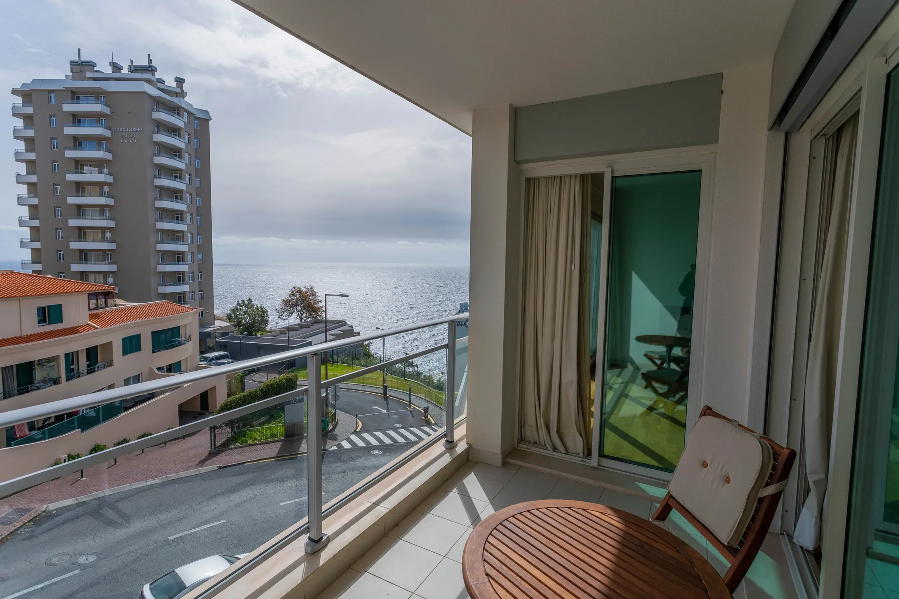 Un balcón embaldosado con asientos da al mar y a edificios cercanos.