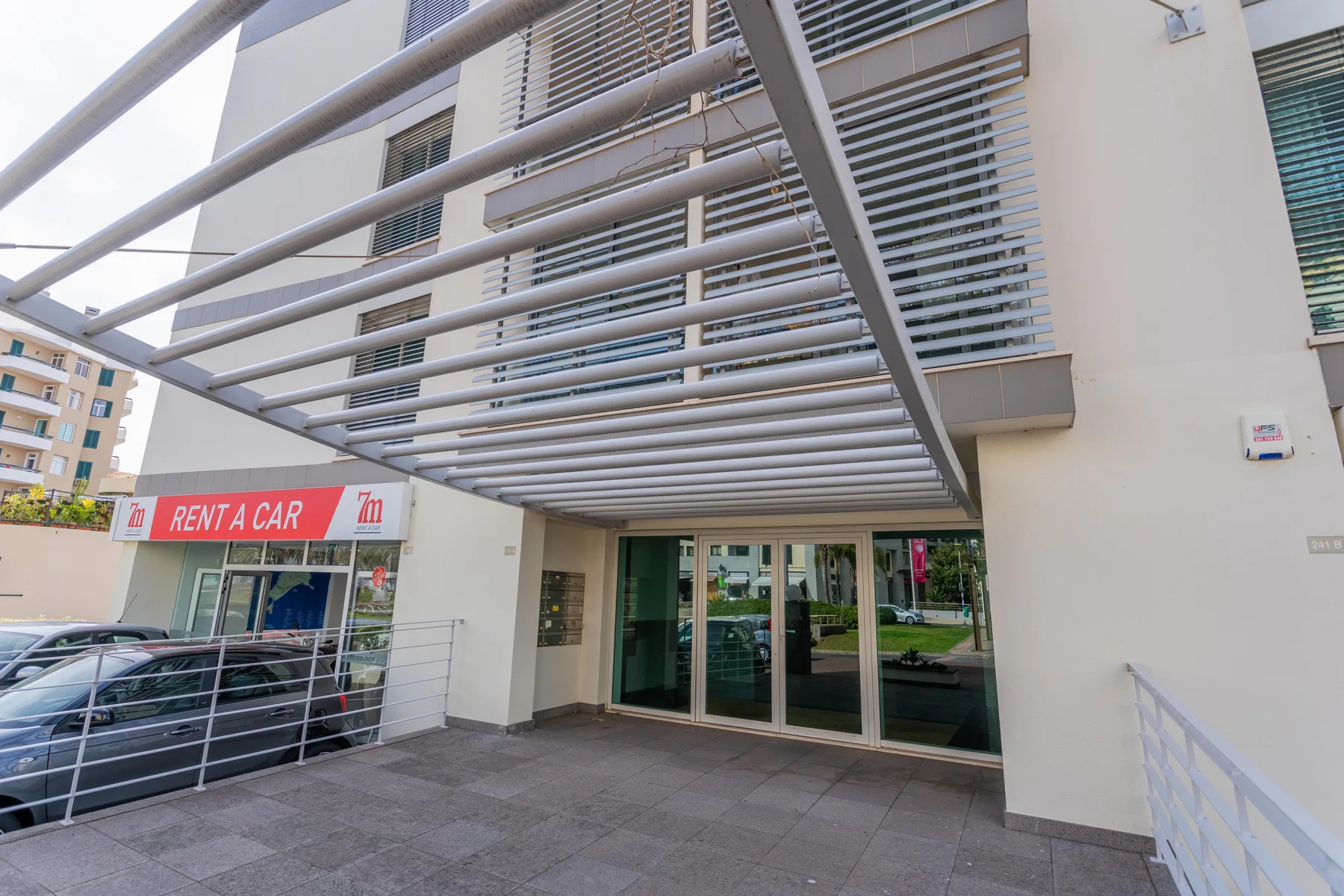 Building entrance beneath a metal canopy, with glass doors and a car rental storefront nearby.