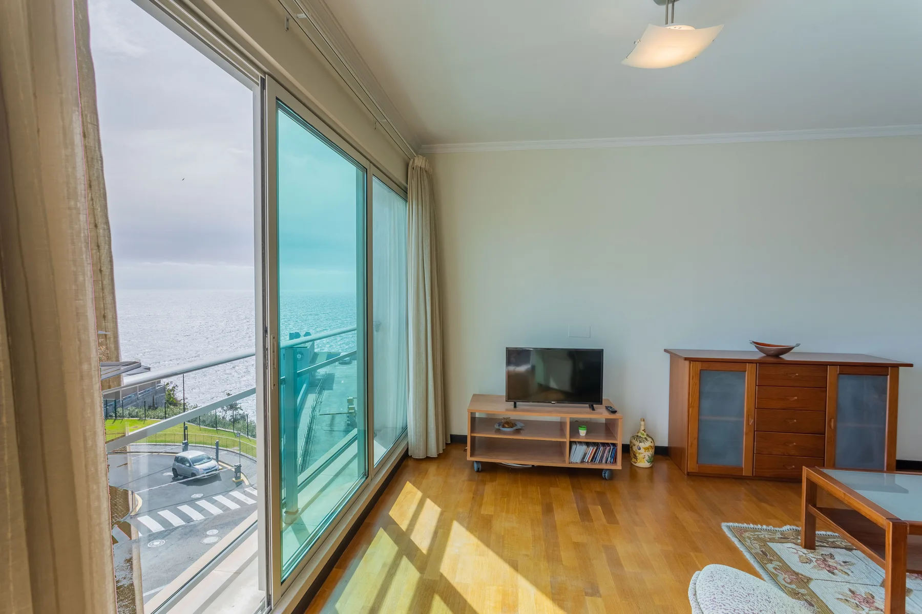 A living room with a television and large glass doors overlooking the sea.