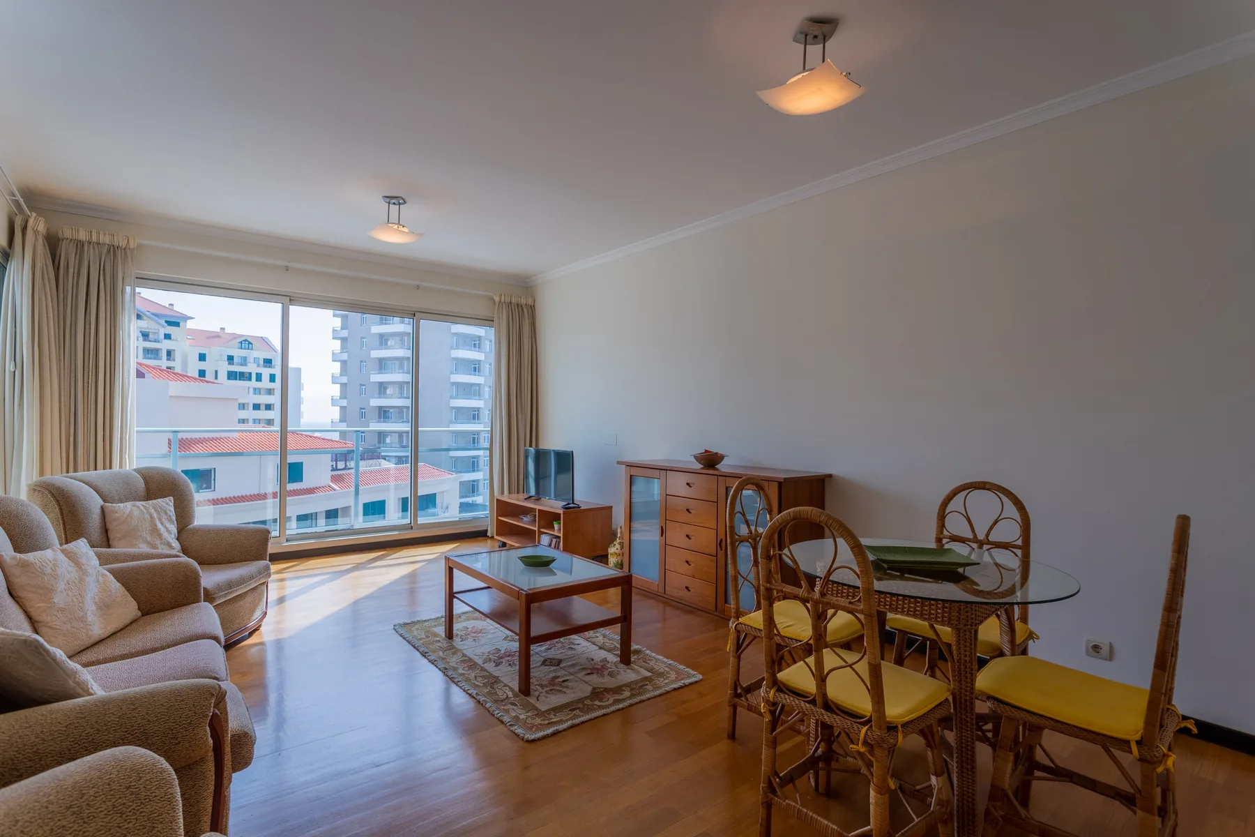 A living and dining room with seating, a glass table, and large windows.