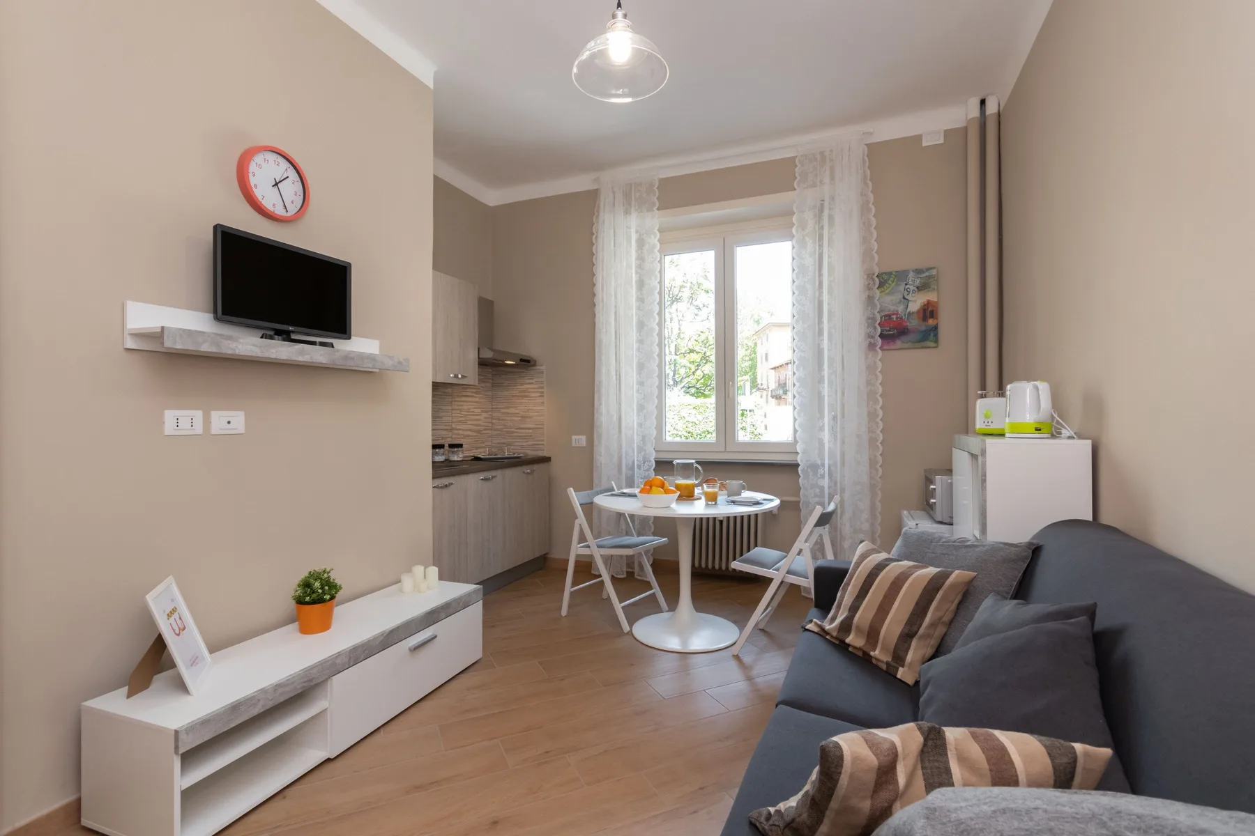 A living room with a sofa, dining table, and kitchenette beside the window.