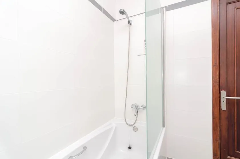 Un baño de azulejos blancos con bañera y ducha.
