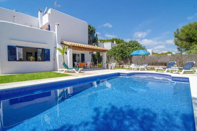 Una piscina está junto a una casa blanca con asientos al aire libre.
