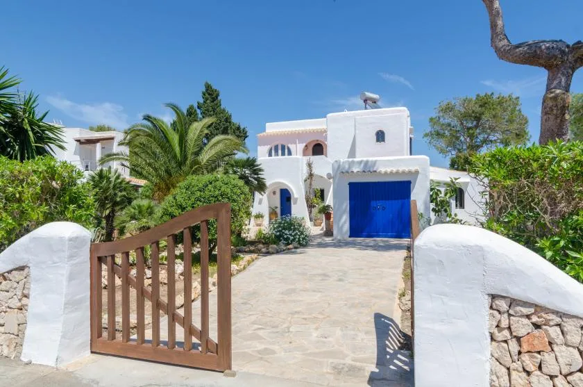 Un edificio blanco con una puerta de garaje azul se alza detrás de una entrada de piedra y una verja abierta.