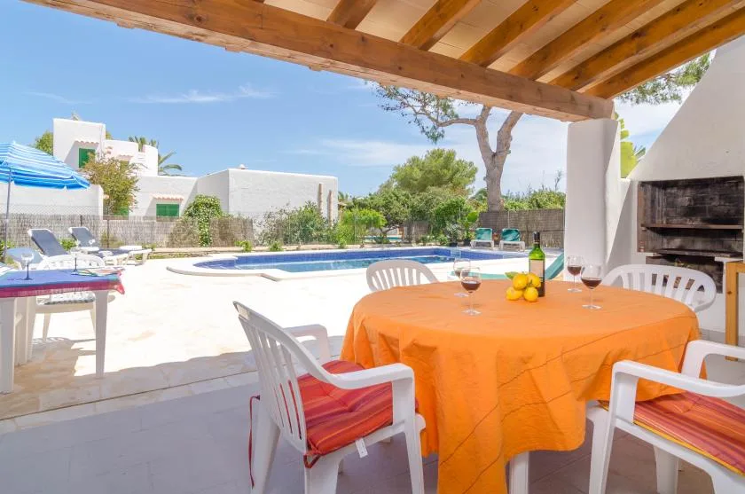 Una zona de comedor exterior cubierta da a una piscina y un patio ajardinado.
