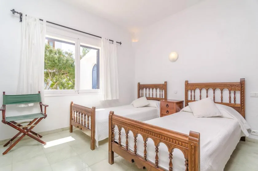 Un dormitorio luminoso con dos camas de madera y una ventana con vistas a la vegetación.
