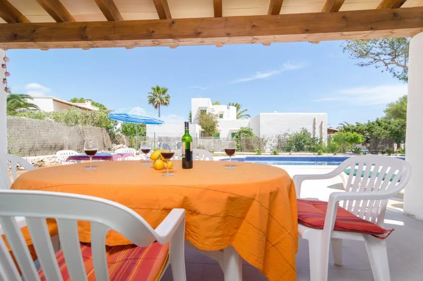 Una zona de comedor al aire libre con sombra y una mesa redonda junto a una piscina.