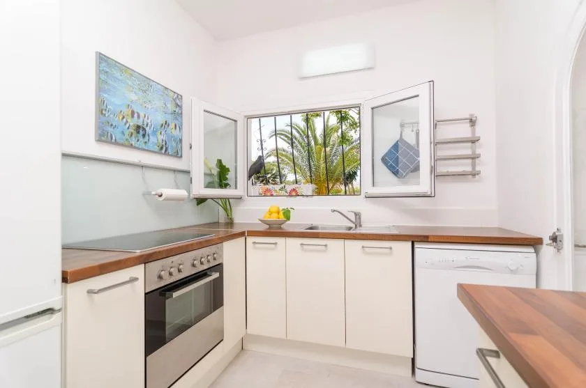 Una cocina luminosa con una encimera de madera y una ventana con palmeras a la vista.