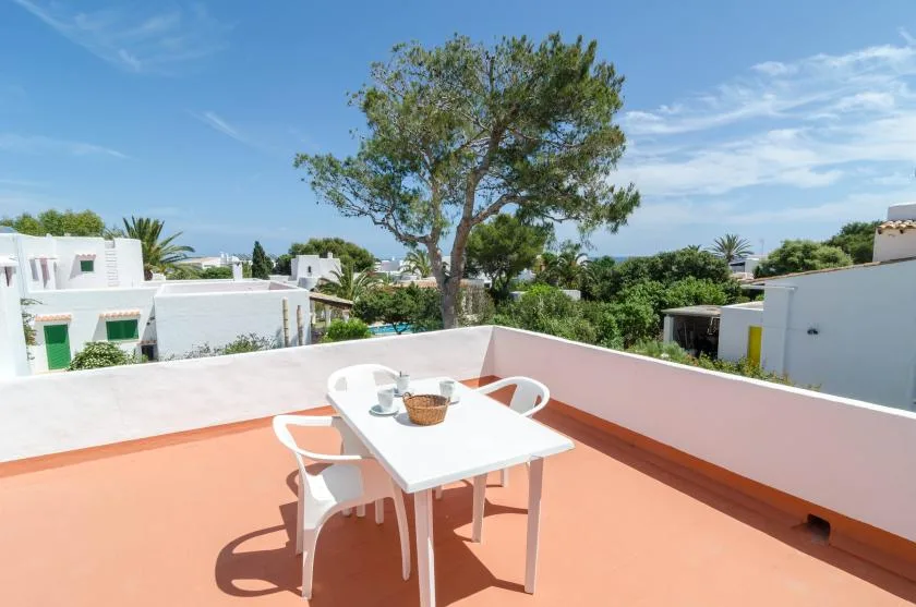Una terraza soleada en la azotea tiene una mesa blanca y sillas.