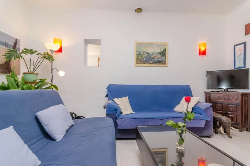 Una sala de estar con asientos azules, una mesa de centro de vidrio y cuadros en la pared.