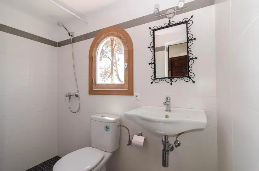 Un baño luminoso con lavabo suspendido, inodoro y ventana arqueada.