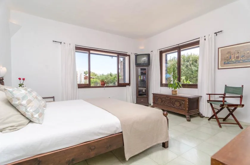 Un dormitorio con una cama, ventanas con cortinas y un baúl de madera.