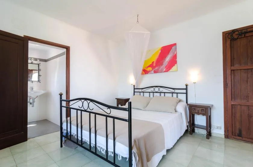 Un dormitorio con una cama de metal, ropa de cama blanca y arte colorido en la pared.