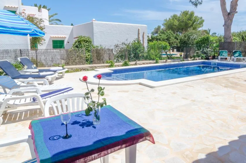 Una piscina está junto a un patio soleado con asientos para descansar.