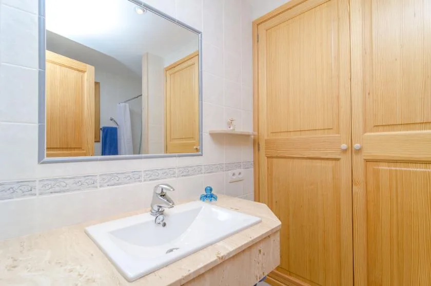 Un baño luminoso con lavabo, espejo grande y armarios de madera.