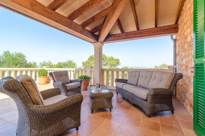 Una terraza cubierta con asientos de mimbre da a árboles y cielo abierto.