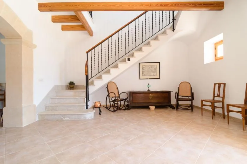 Un pasillo interior luminoso cuenta con una escalera, un baúl de madera y asientos.