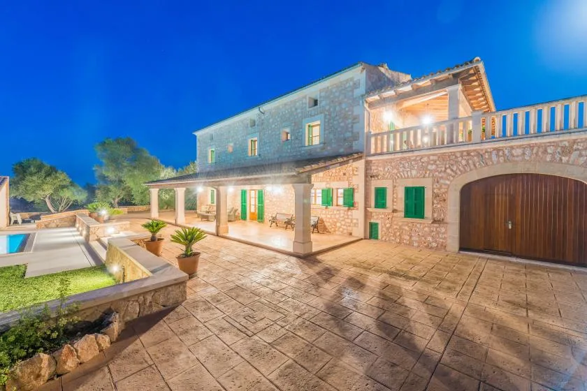Una casa de piedra da a un patio pavimentado con una terraza cubierta.