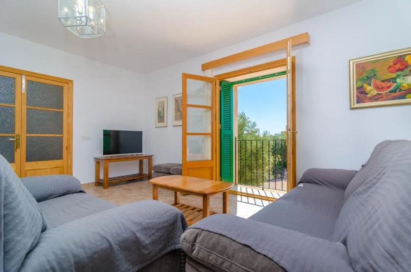 Una sala de estar con asientos grises, una mesa de centro de madera y una puerta abierta al balcón.