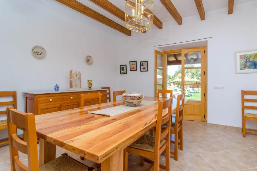 Comedor con una mesa larga de madera y sillas bajo vigas expuestas.